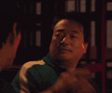 a man in a green jacket with white stripes is talking to another man in a dark room