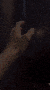 a person 's hand is reaching out towards a black refrigerator door .