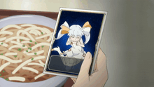 a person holding a picture of a girl with a bow in front of a bowl of noodles