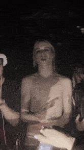 a man without a shirt is standing in a dark room with other people