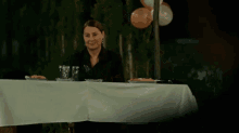 a woman sits at a table with plates of food and balloons behind her