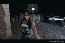 a woman in a green dress is holding a box in her hands and a car is behind her on makeagif.com