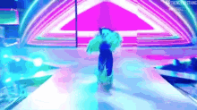 a woman in a green dress is walking down a runway on a stage in front of a purple and blue background .