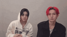 two young men with red hair are sitting next to each other in front of a wall .