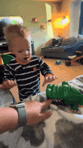 a little boy in a striped shirt is playing with a toy crocodile