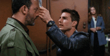 a man in a leather jacket is touching another man 's face in a room .