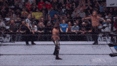 a group of wrestlers are standing in a wrestling ring with a referee and a crowd watching .