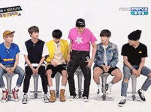 a group of young men are sitting on stools in front of a mbc channel sign .