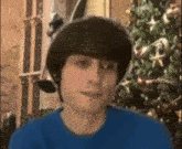 a young man in a blue shirt is standing in front of a christmas tree and smiling .