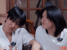 two young men sitting next to each other with one wearing a shirt that says x