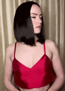 a woman in a red crop top stands in front of a curtain