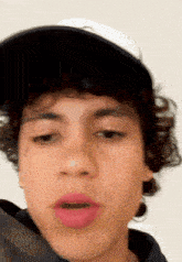 a young man with curly hair is wearing a baseball cap