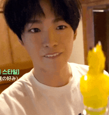 a young man in a white shirt is smiling and holding a yellow object in front of a sign that says " ae "