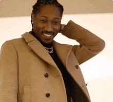 a man in a tan coat is smiling and touching his head .