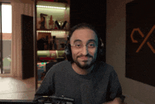 a man wearing headphones and glasses looks at the camera in front of a sign that says %