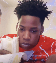 a man in a red shirt is eating a burrito