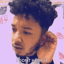 a man with curly hair is holding his hand to his ear and saying `` i dont hear it ''