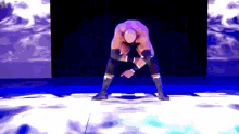 a wrestler is kneeling down on a stage with his hands in his pockets