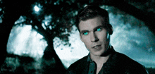 a man with blue eyes is standing in front of trees