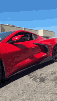 a man is driving a red sports car on a street .
