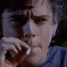 a close up of a man smoking a cigarette in a blue shirt .