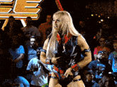 a woman in a wrestling outfit stands in front of a crowd and a sign that says e