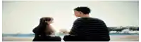 a man and a girl are sitting on the beach holding hands .