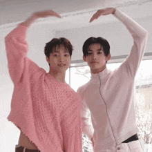 two young men wearing pink sweaters are making a heart with their hands