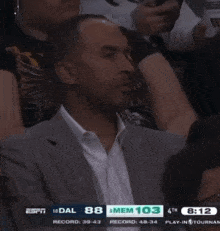 a man in a suit sits in the stands watching a basketball game with espn on the screen