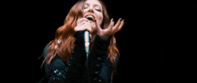 a woman with red hair is singing into a microphone in a dark room