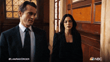a man in a suit and tie stands next to a woman in a black dress and a nbc logo