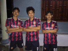 three boys wearing emirates jerseys stand with their arms crossed in front of a window