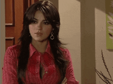 a woman wearing a red shirt and earrings is standing in a room