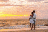 a man and a woman are standing on a beach looking at the ocean at sunset .