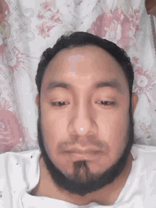 a man with a beard is laying on a bed with a floral pillow