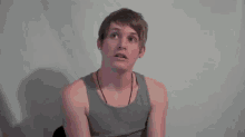 a young man is wearing a gray tank top and a necklace .