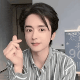 a young man wearing a striped shirt is making a heart shape with his hands .