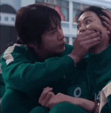 a woman is covering another woman 's mouth with her hands while sitting next to her .