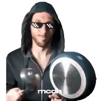 a man wearing a hoodie and sunglasses is holding a pan and a spoon and the word mcah is on the bottom right
