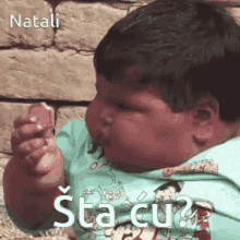 a little boy is eating a cookie and making a funny face with the words natali sta cu written above him .
