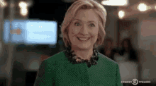 hillary clinton is smiling while wearing a green dress and necklace .