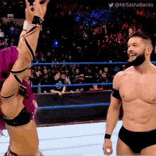a man and a woman are standing in a wrestling ring and the woman is wearing a pink top