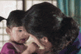 a woman is holding a baby in her arms and the baby is looking at the camera