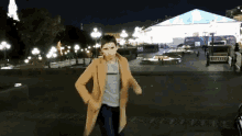 a man in a tan coat is dancing in front of a large building that says ' russia ' on it