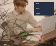a man is sitting at a desk with a laptop and a mute block and report button