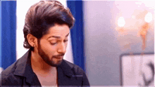 a man with a beard wearing a black shirt and earrings is looking down .