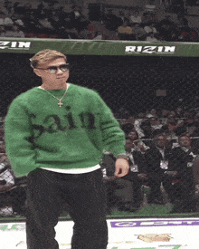a man in a green saint sweater stands in front of a rizin banner
