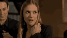 a woman in a black jacket has her hand on her face
