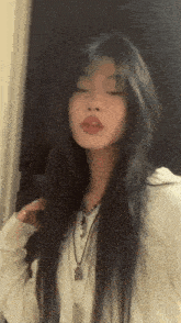 a woman with long dark hair is wearing a white sweater and necklaces .