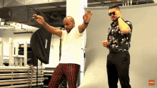 a man in plaid pants stands next to another man wearing sunglasses